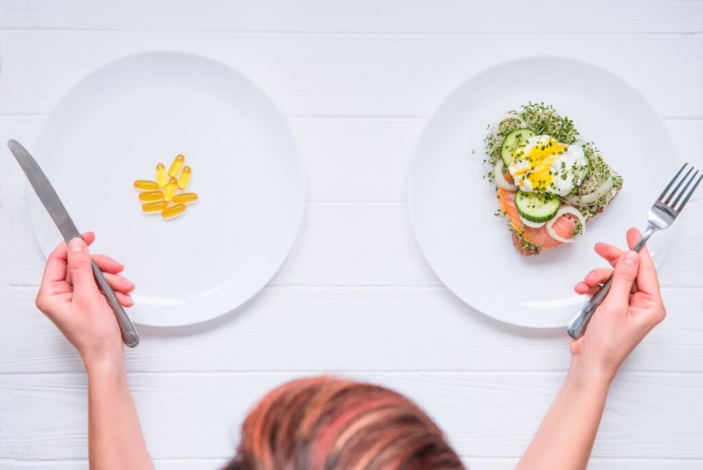 Top view woman with cutlery in hands choosing between healthy food or medical pills on the plate