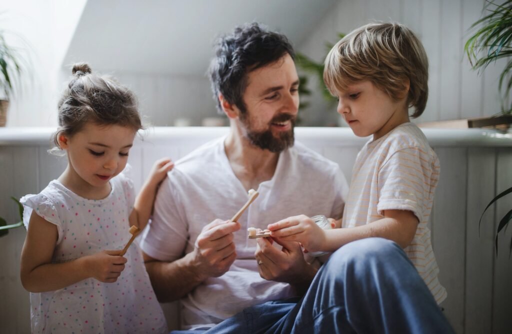 Father with two small children brushing teeth indoors at home, sustainable lifestyle concept