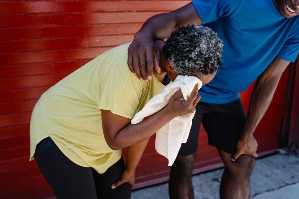 Man in Blue Shirt Assisting the Woman in Yellow Shirt while Wiping Her Sweat