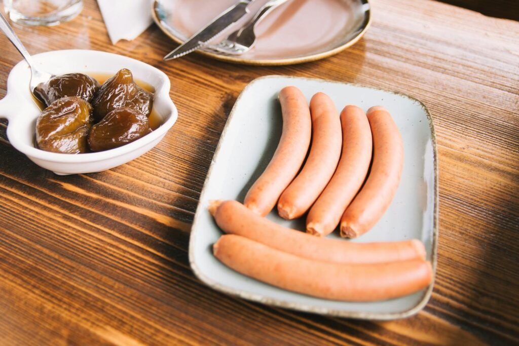 Plate of sausages with a side of figs on a rustic wooden table. Perfect food photography for culinary themes.