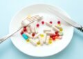 Many different weight loss pills and supplements as food on round white plate with fork and knife