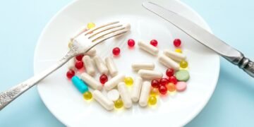 Many different weight loss pills and supplements as food on round white plate with fork and knife