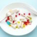 Many different weight loss pills and supplements as food on round white plate with fork and knife