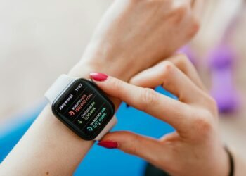 Unrecognizable female with manicure checking smartwatch on hand while sitting on yoga mat