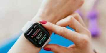 Unrecognizable female with manicure checking smartwatch on hand while sitting on yoga mat